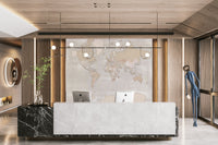 Rustic World Map wallpaper in warm beige behind a white marble reception desk with two iMacs in an office lobby