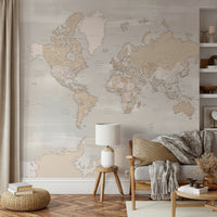 Rustic World Map wallpaper in beige behind a wood-frame sofa with mustard cushion and a lamp on a stool in a living room