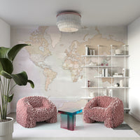 Rustic World Map wallpaper in pastel tones behind blush pink feathered armchairs and white shelves in a living room