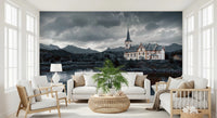 Sacred Shores wallpaper mural of a lakeside church under storm clouds behind two white sofas and a palm in a living room