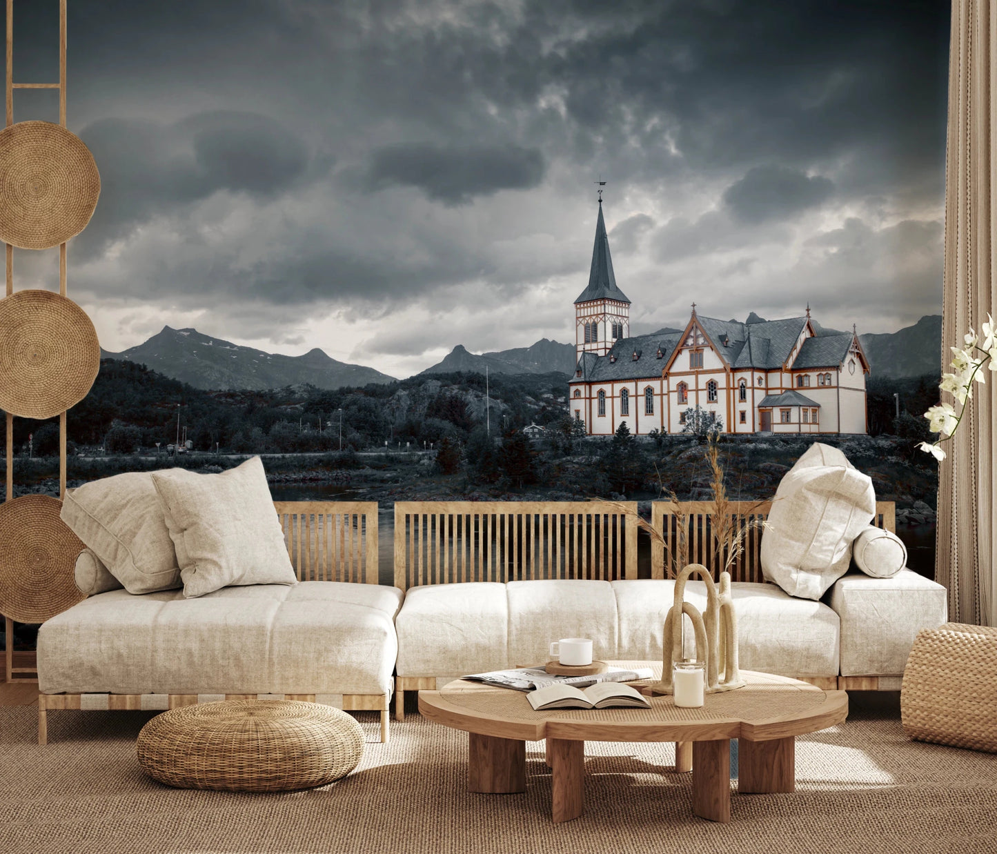 Sacred Shores wallpaper mural of a church under grey clouds behind a cream linen sofa and rattan pouf in a living room