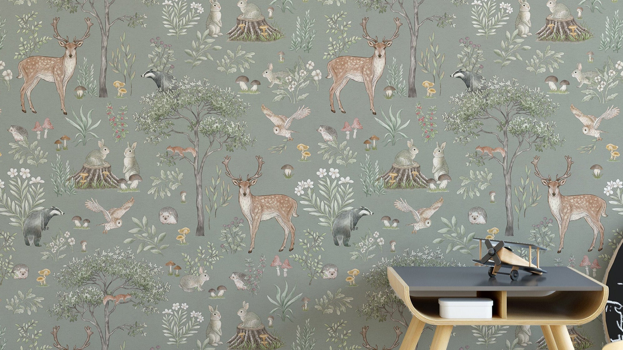 Sage Green Wildlife wallpaper with deer, badgers and owls behind a dark wood side table in a kids room