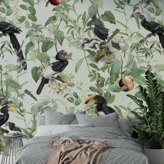 Savannah wallpaper mural with hornbill birds and green foliage behind a grey quilted bed and potted fern