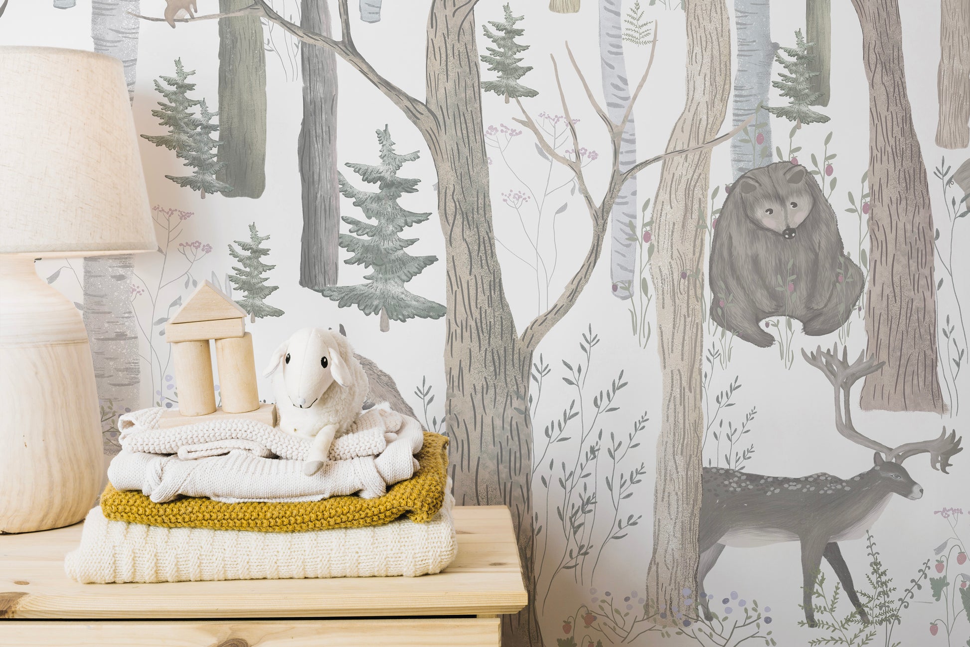 Mystical Forest Scene wallpaper mural of watercolor birch woods with a bear and deer beside stacked knit blankets and a lamb plush