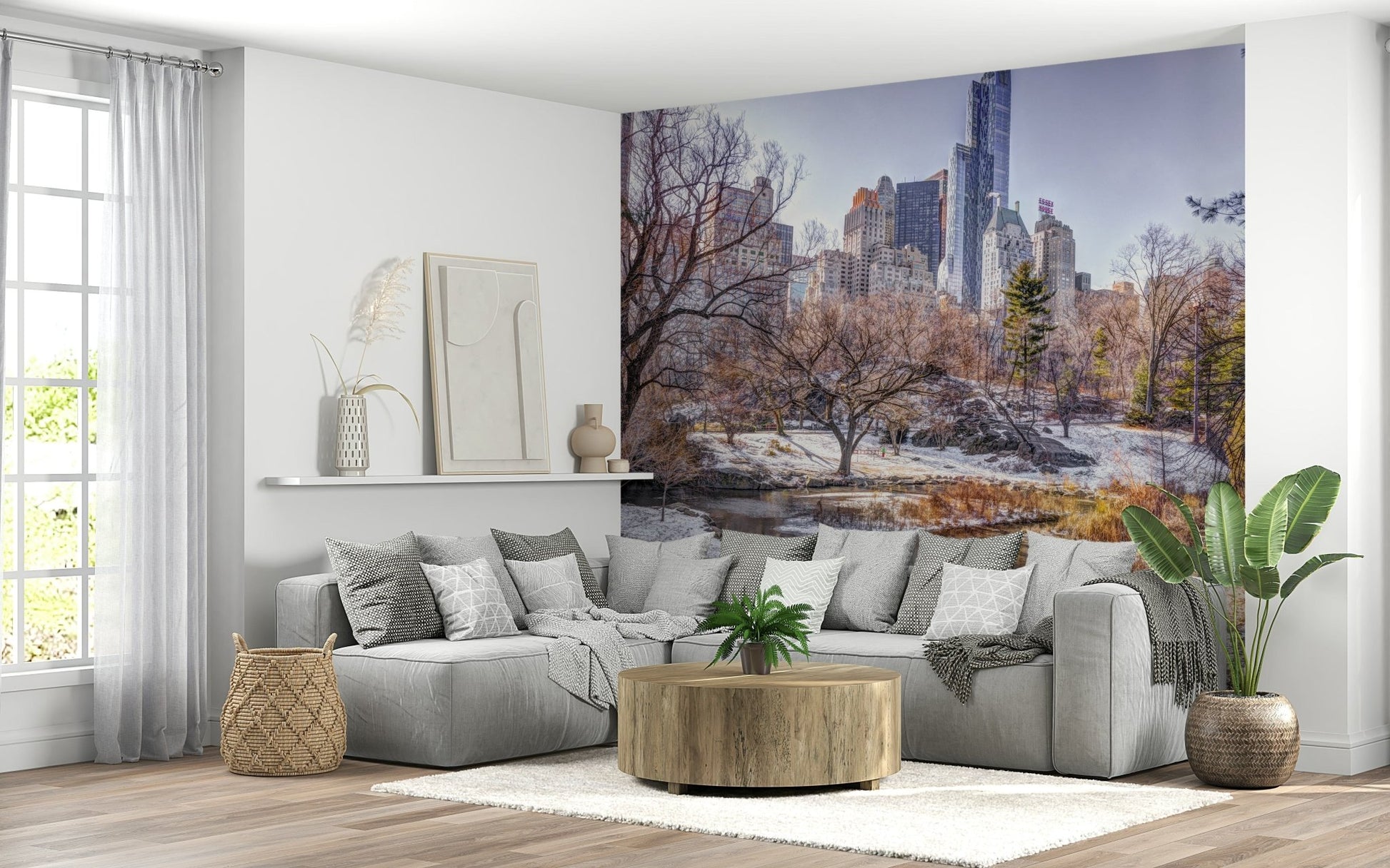 Snowy Central Park mural with bare trees and skyline above a grey L-sectional and round wood coffee table