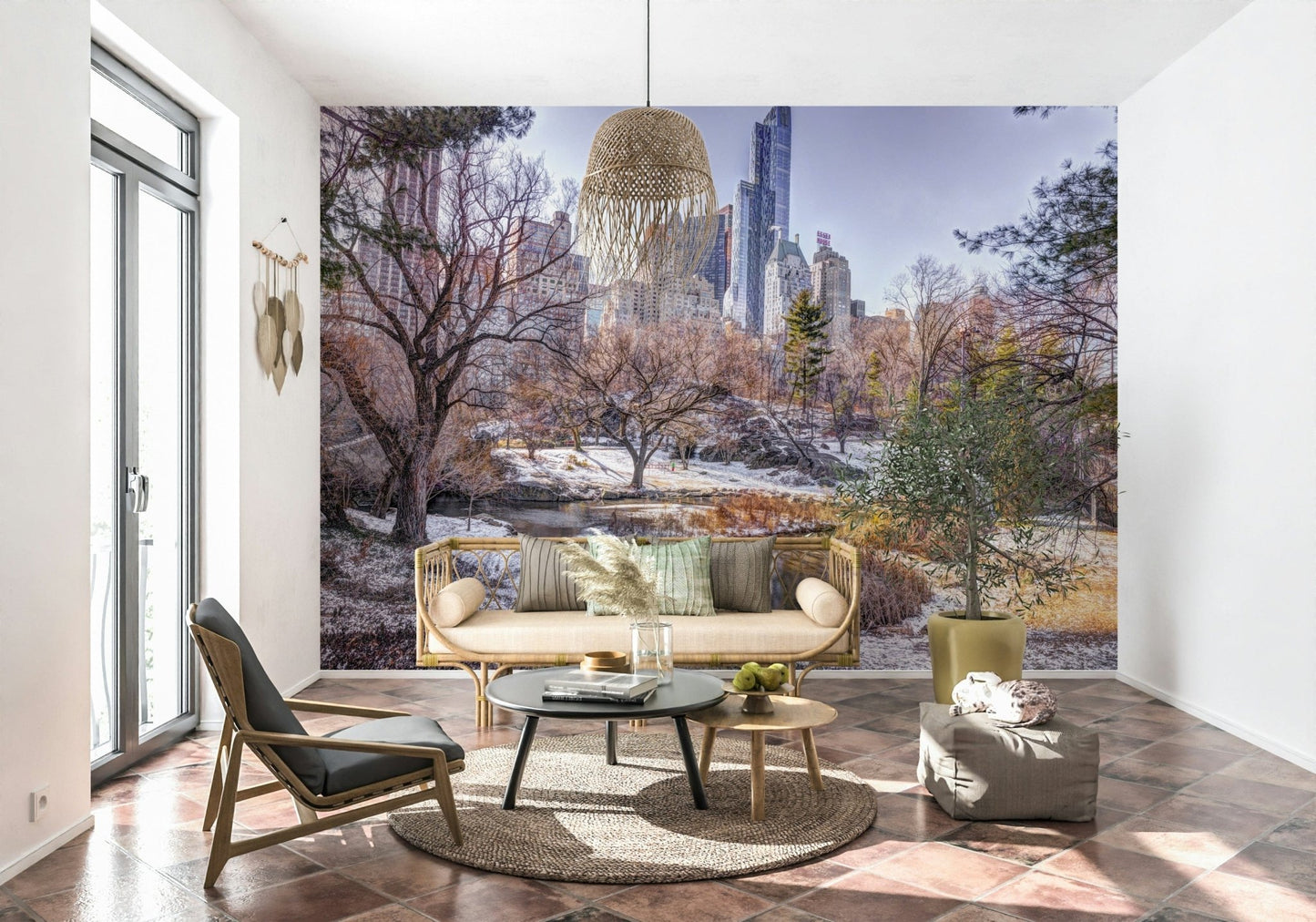 Snowy Central Park mural behind a rattan sofa with round black and wood tables and a potted olive plant