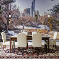 Snowy Central Park mural over a wood dining table and cream chairs on a red Persian rug with wall sconces