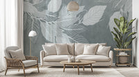 Elegant Teal Botanical Leaf wallpaper mural with pale leaves behind a cream sofa and woven armchair in a living room