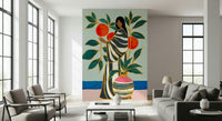 The Keeper of Oranges wallpaper mural of a woman with an orange tree behind a gray sofa and armchairs by tall windows