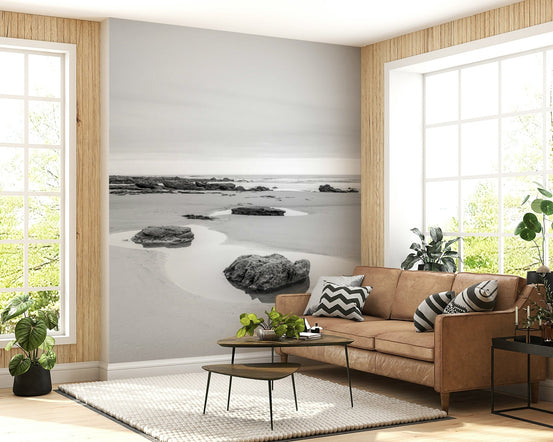 Tide Pools black and white wall mural of rocks on pale sand behind a tan leather sofa in a bright living room