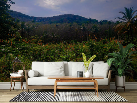 Tropical Canopy wallpaper mural showing green jungle hills and orange flowers behind a white sofa in a living room