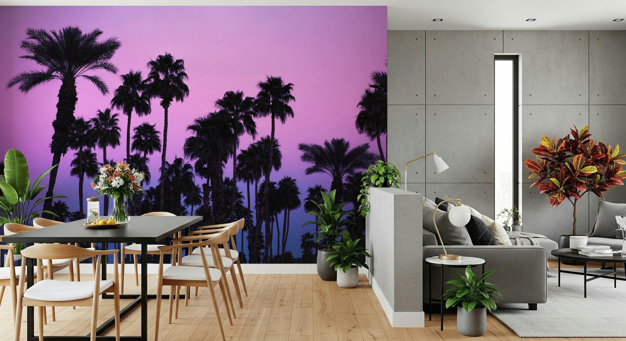 Tropical Dusk Palms wallpaper mural of palm silhouettes against a pink sunset behind a dark dining table beside a grey-sofa living area