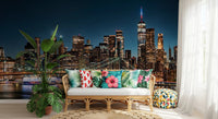 Urban Nightscape wallpaper mural behind a rattan sofa with tropical hibiscus cushions and leafy plants