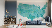 USA map with states and capitals in teal watercolor wallpaper mural in a kids bedroom with a navy bed and rocket toy