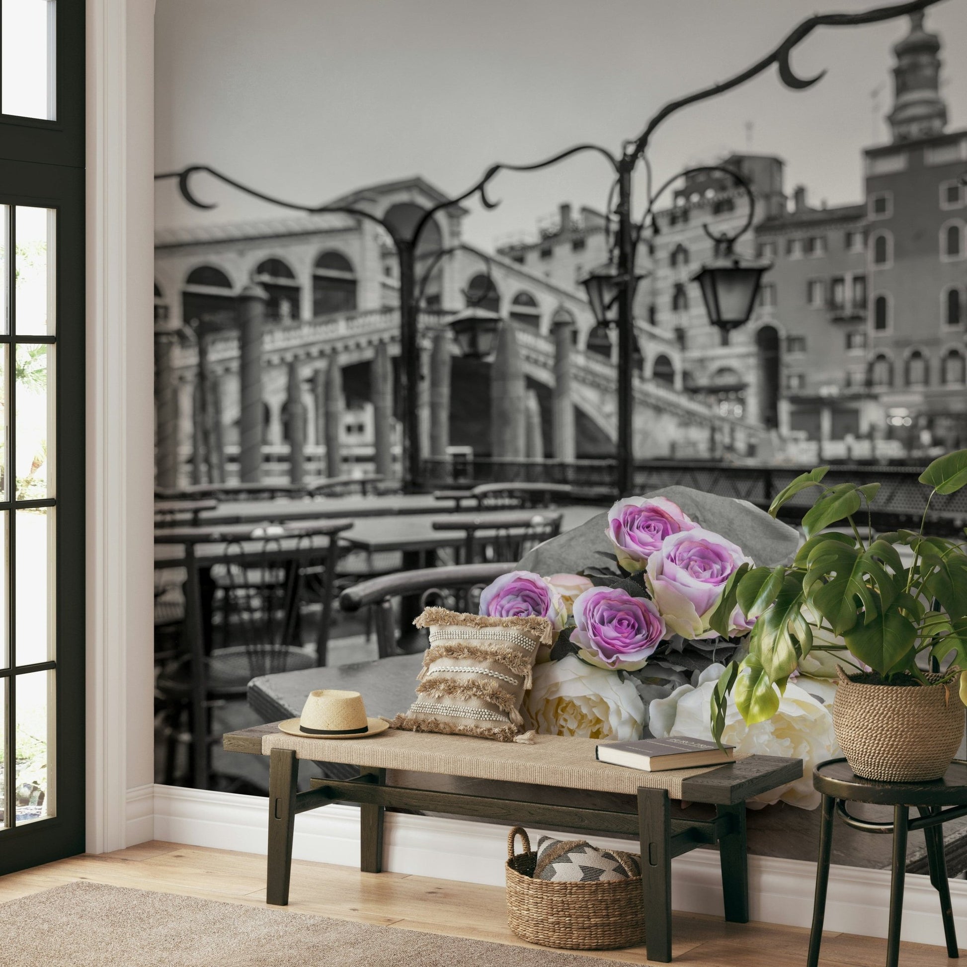 Venetian Blooms wallpaper mural with grey Venice bridge and roses behind a wooden entryway bench, sun hat and potted plant