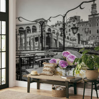 Venetian Blooms wallpaper mural with grey Venice bridge and roses behind a wooden entryway bench, sun hat and potted plant