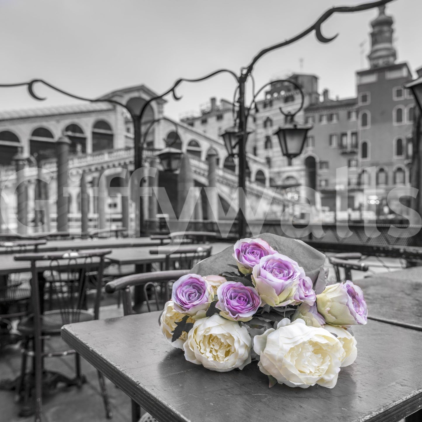 Venetian Blooms wallpaper mural close-up showing pink and cream roses on a cafe table before the monochrome Venice Rialto Bridge