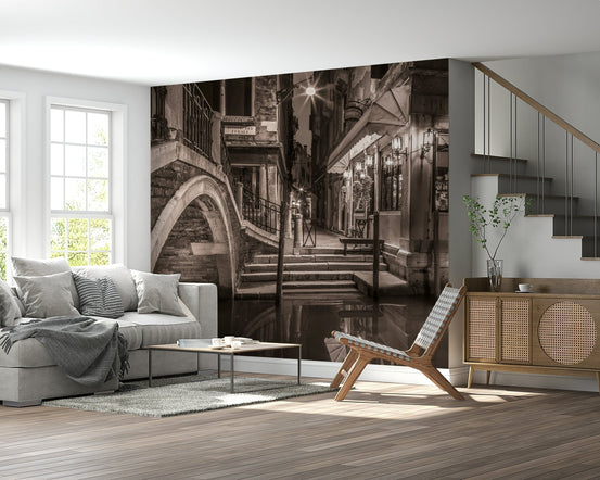 Venetian Canals wallpaper mural of a sepia Venice canal bridge behind a grey sofa beside a wood staircase and sideboard