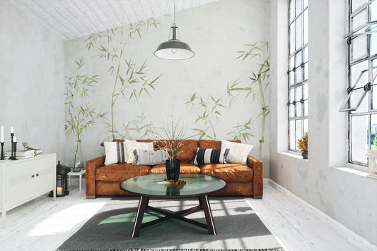Watercolor Bamboo Tree wallpaper mural in soft green behind a tan leather sofa in a sunlit living room