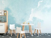 Watercolor Sky Clouds wallpaper mural in soft blue behind a white play kitchen in a kids playroom