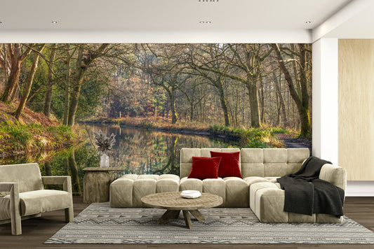 Woodland Mirror wallpaper mural with a forest reflected in still water behind a beige sectional sofa and red cushions in a living room