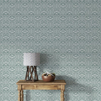 Zenith Leaves wallpaper in teal green shown above a rustic wood console table with a lamp in an entryway